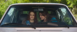 Crítica Prácticamente magia 2 (Susanne Bier, 2026) 11 Joey King en el asiento del copiloto en la izquierda y Maisie Williams en la derecha en el asiento del piloto mirando a un móvil con carcasa azul